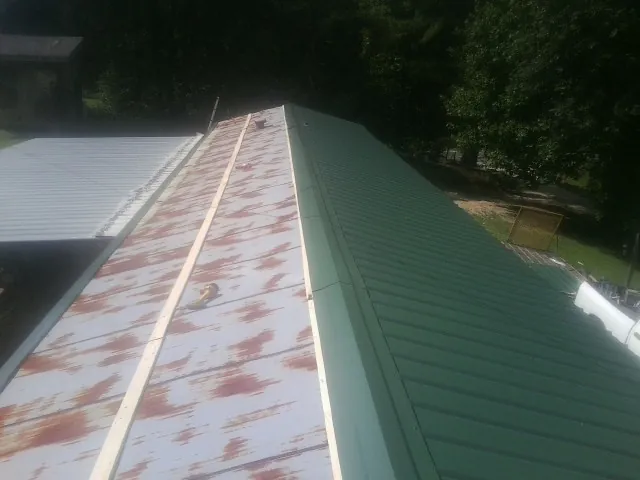 Old rusted panels beside newly installed green metal roofing — Wind Damage Roof Repair by Roofing Brothers in Ossian