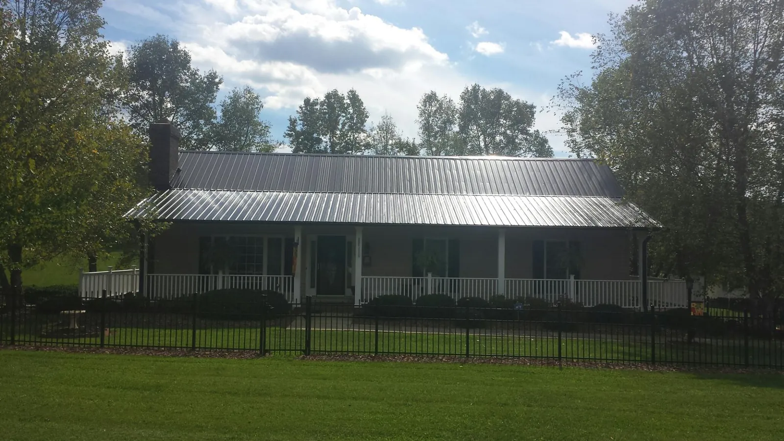 Gray metal roof on a brick ranch with a full width front porch — Gutter Guard Installation work by our crew in Ossian