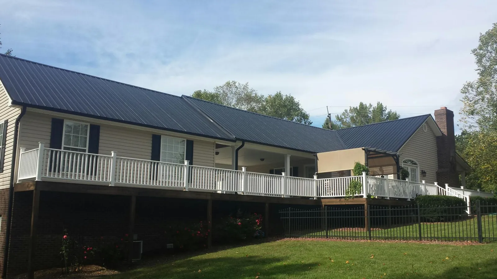 Black metal roof above a long white railed deck on a hillside home in Ossian