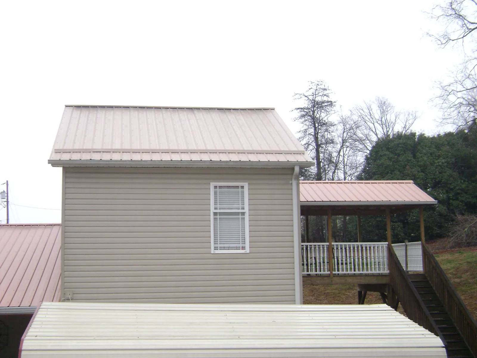 Tan metal roofs on a two story addition and attached porch, from a Roof Replacement job in Ossian